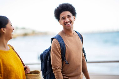 İki mutlu arkadaşın portresi deniz kenarında çantasıyla yürüyor.