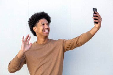 Havalı Afro-Amerikan Adam beyaz duvarda cep telefonuyla selfie çekiyor.