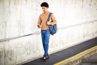 Cep telefonu ve çantasıyla yürüyen tam vücut portresi.