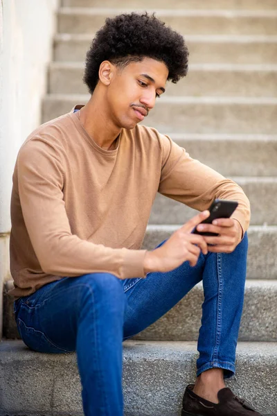 スマートフォンで階段に座っている若いヒスパニック男性の肖像画 — ストック写真