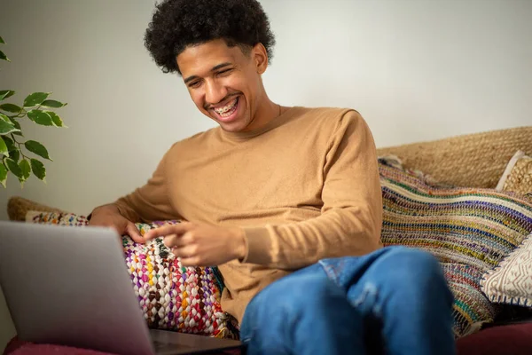 快乐的年轻人坐在家里拿着笔记本电脑 免版税图库照片