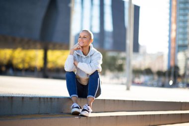 Kafası tıraşlı bir kadının tüm vücudu merdivenlerde oturuyor.