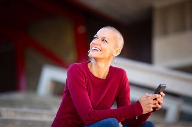 Elinde cep telefonuyla oturan gülümseyen kadının portresi.