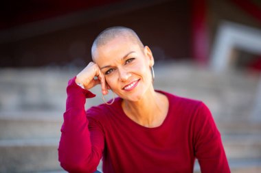 Kafası tıraşlı, gülümseyen bir kadının portresi.