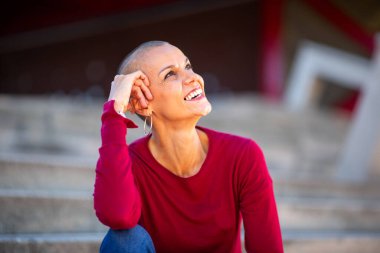 Kafası tıraşlı, gülümseyen ve başka tarafa bakan bir kadının portresi.