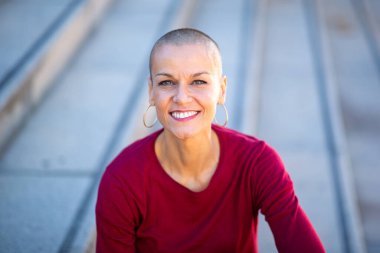 Kafası tıraşlı, gülümseyen bir kadının yakın portresi.