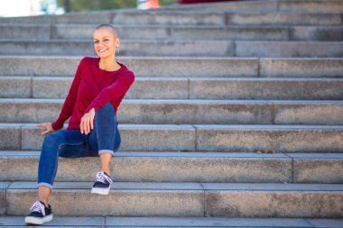 Tıraşlı saçlı, merdivenlerde oturan kadın portresi.