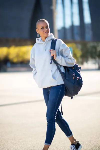 Portrait of shaved head woman walking in city with bag