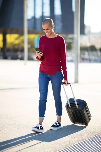 Full body portrait of travel woman walking with mobile phone and suitcase in city