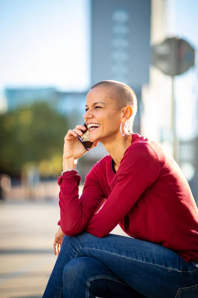 Portrait of shaved head woman talking with cellphone in the city