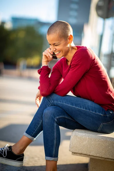 Portrait of smiling shaved head woman talking with cellphone in the city