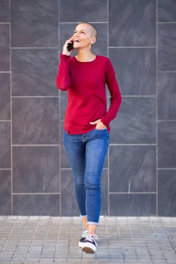 Tıraşlı saçlı, yürüyen ve cep telefonuyla konuşan kadın portresi.