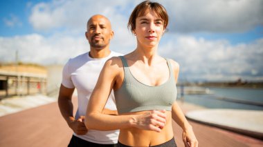 İki koşu partnerinin manzaralı bir rıhtımda volta atması gibi odaklanmış ve enerjik bir an. İfadelerindeki kararlılıkla, sağlıklı ve aktif bir yaşam tarzının özünü somutlaştırıyorlar..