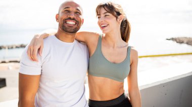 Neşeli çift okyanus kenarında aktif yaşam tarzlarını kucaklıyor, güneşli bir açık hava spor salonunda mutluluk ve motivasyon yayıyorlar..