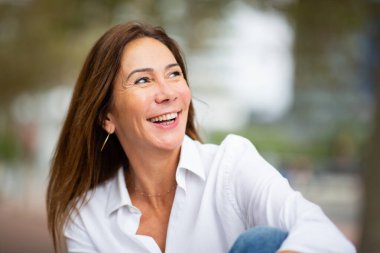 Beyaz gömlekli, gülümseyen bir kadını gösteren neşeli ve doğal bir portre.