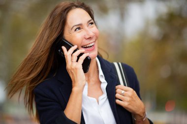 Parkta yürürken canlı bir telefon konuşması yapan neşeli bir kadının yakın plan portresi.