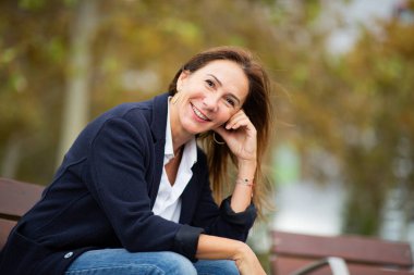 Bir bankta oturan kadın, kendine güveni ve çekiciliğiyle gülümsüyor.