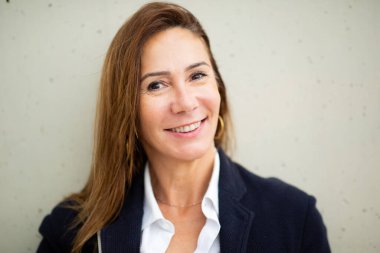 Beyaz duvarda gülümseyen kendine güvenen bir kadın portresi.