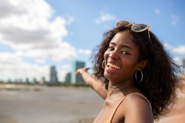 Kıvırcık saçlı, gülümseyen siyah kadın şehir ortamında selfie çekiyor..