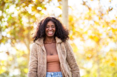 Parkta sonbahar boyunca gülümseyen Afrikalı genç bir kadın portresi