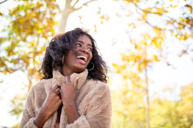 Açık havada ceketle gülen genç zenci kadın portresi.