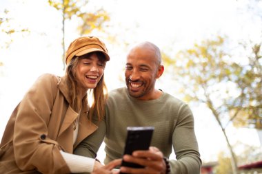 Parkta cep telefonuna bakan gülen adam ve kadın portresi.