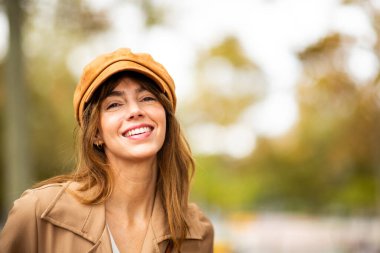 Paltolu ve şapkalı gülümseyen genç bir kadın kameraya bakıyor.