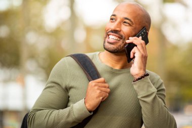 Dışarıda cep telefonuyla konuşurken gülümseyen kendinden emin bir adam portresi.