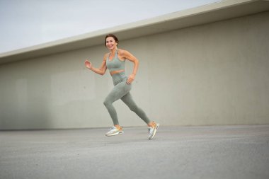 Uzun boylu, gülümseyen, spor yapan bir kadın şehir dışında koşuyor.