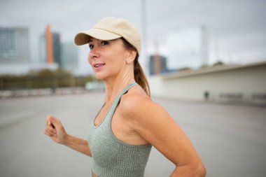 Kenar manzaralı kadın koşucu şehir merkezinde şapka takıyor.