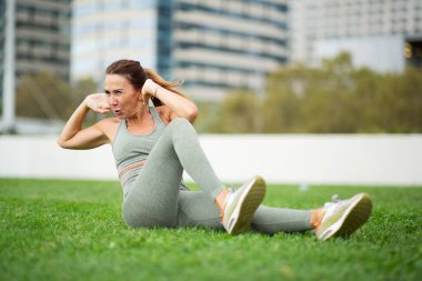 Park alanındaki çimlerde mide egzersizi yapan yaşlı kadın portresi.