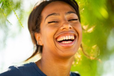 Açık havada gülen neşeli kadın, yumuşak yeşilliklerle çevrili.