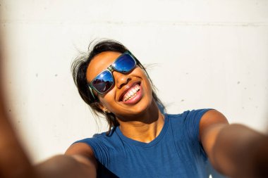 Neşeli genç bir kadın beyaz arka planda selfie çekiyor.