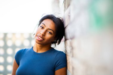 Genç bir kadın başını duvara yaslıyor ve kameraya bakıyor.