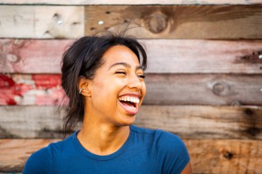 Renkli bir duvarın önünde gülen neşeli genç bir kadın.