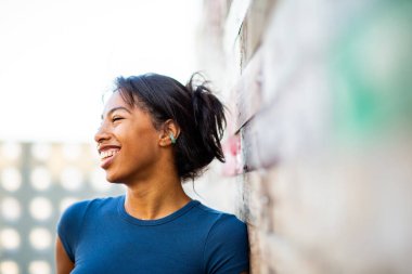 Gülümseyen genç bir kadın duvarın önünde duruyor ve başka tarafa bakıyor.