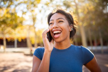 Açık havada telefonla konuşurken gülen genç siyahi bir kadının portresini yakından çek.