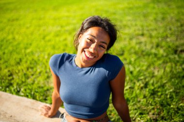 Yeşil tarlada oturan genç bir kadının neşeli portresi.