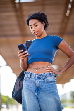 Şehirde ayakta duran ve cep telefonuna bakan genç bir kadının portresi.