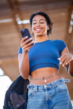 Dışarıda telefonuna gülümseyen genç bir kadın.