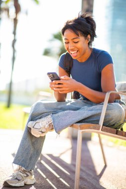 Şehirde bankta oturan, cep telefonu kullanan genç bir kadının portresi.