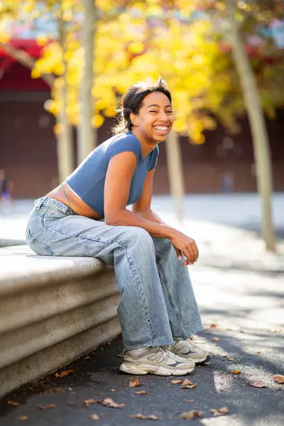 Genç bir kadının tüm vücudu beton bir bankta oturmuş gülüyor.