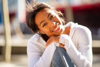 Neşeli genç bayanı yakın, gün ışığında dışarıda oturuyor.