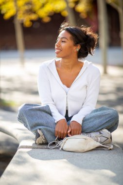 Güneşli bir günde, açık havada oturmuş, gülümseyen genç bir kadının portresi.