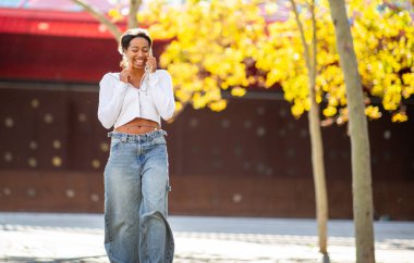 Tam vücut genç kadın cep telefonuyla yürüyor ve konuşuyor.