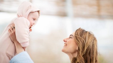 Neşeli anne, gülümseyen bebeğini kaldırırken göz teması kuruyor.
