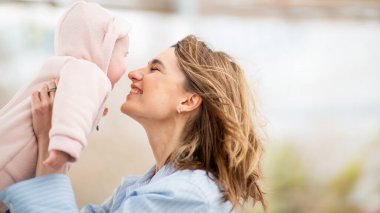 Anne bebeğini kucağında tutuyor, burunlarına dokunurken gülümsüyor açık havada sevgi dolu bir anda..