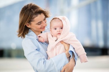 Anne bebeğine sevgiyle bakıyor, o da rahat pembe bir tulum giymiş ve kapüşonlu.