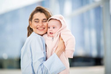 Gülümseyen annenin portresi açık havada pembe kapüşonlu bebeğini kucaklıyor.