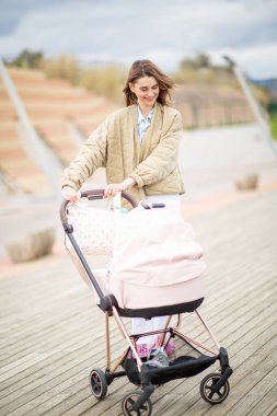 Gülümseyen kadın bebek arabasını iterken tahta kaldırımda yürümekten hoşlanır.